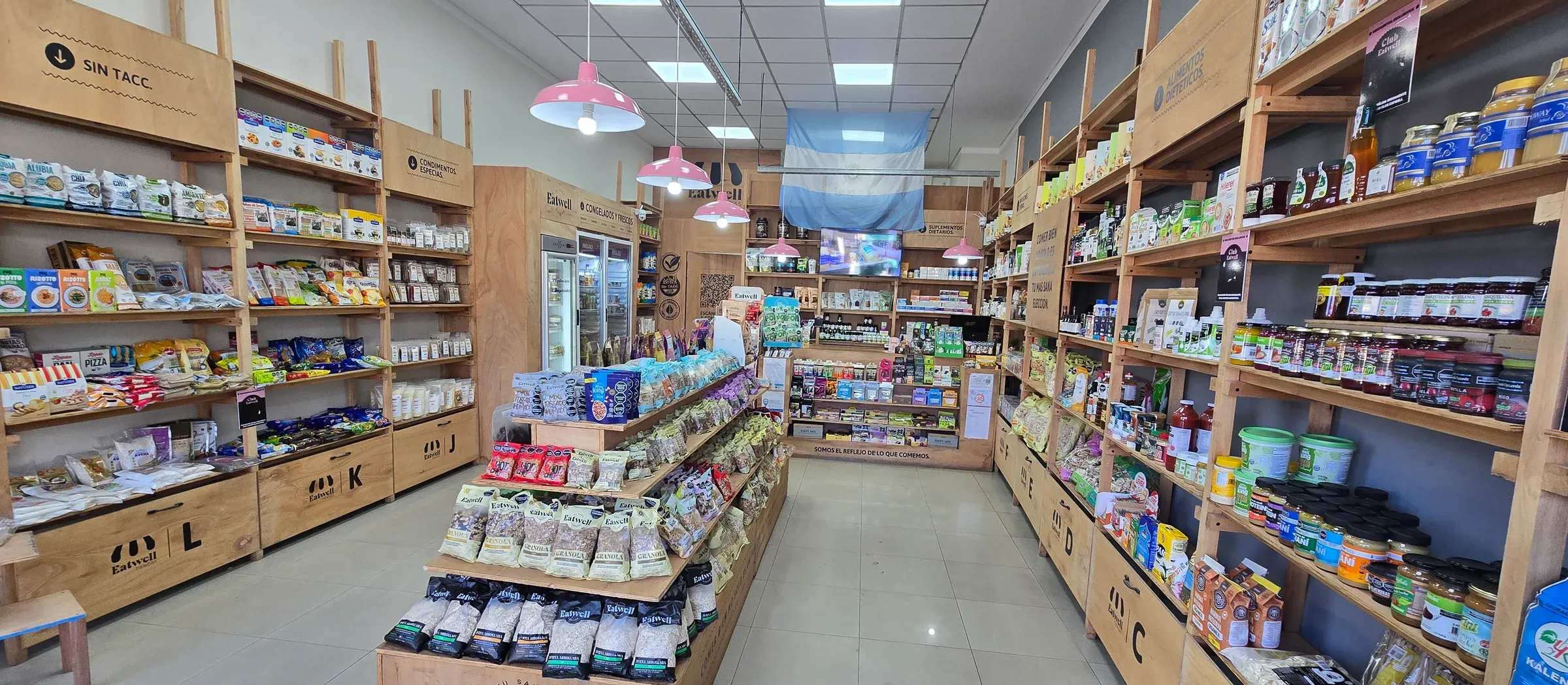 Interior de la Tienda Eatwell de Catamarca: dos paredes de góndolas de madera y una isla central con granolas y frutos secos fraccionados.