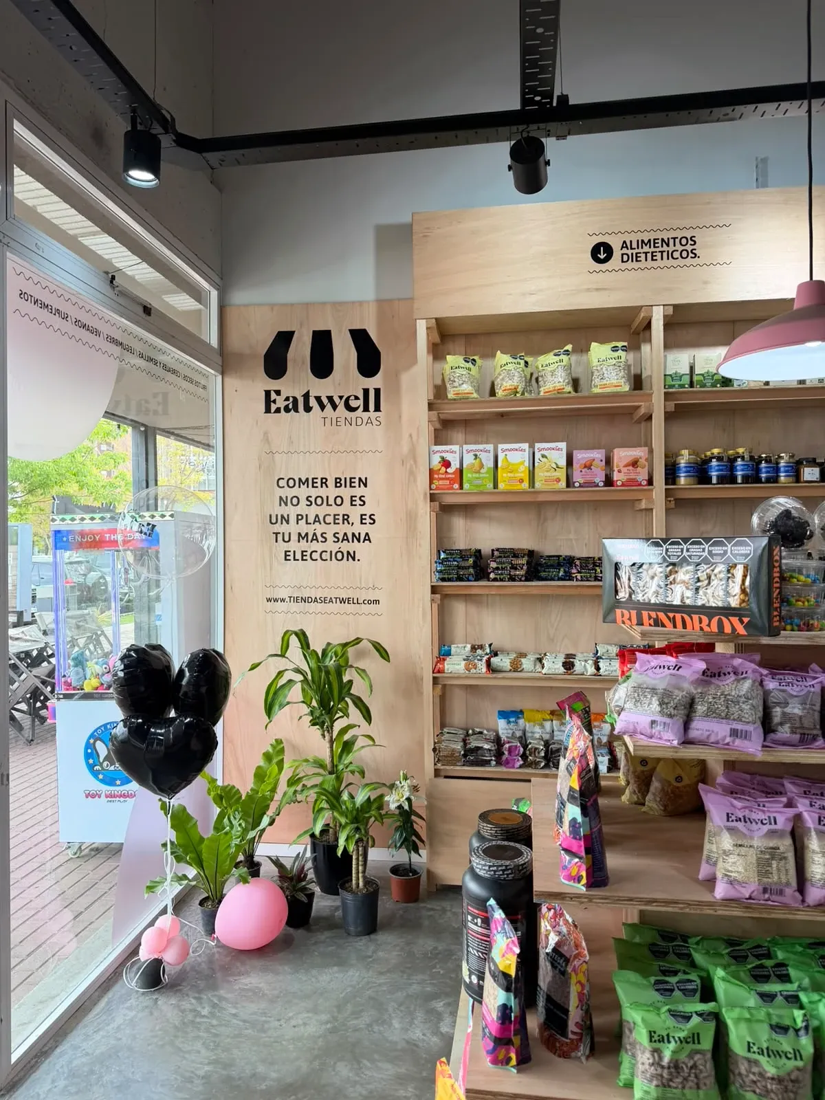 Interior de la Tienda Eatwell de Santa Fe 2, junto a la vidriera, con el cartel "Comer bien no solo es un placer, es tu más sana elección" y góndolas de alimentos dietéticos.